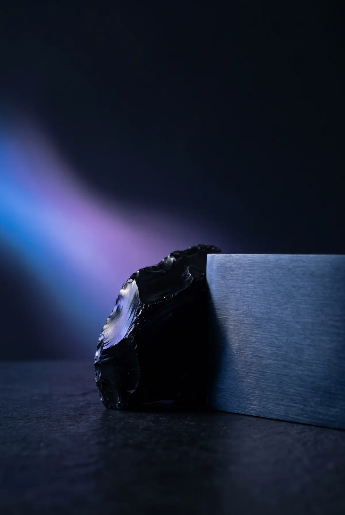 Obsidian and brushed metal lit by a soft blue and violet wash — human intuition meeting machine precision